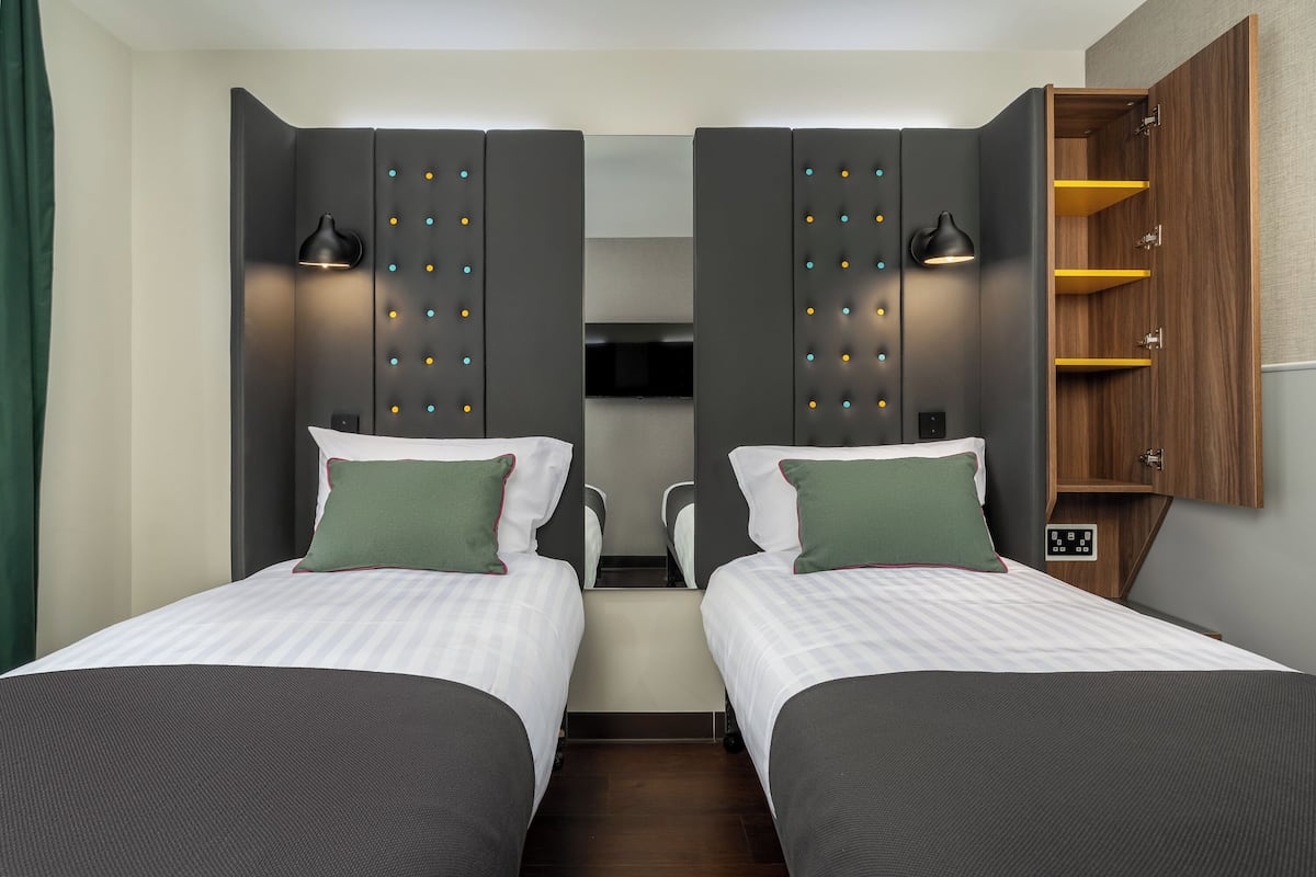 Habitació d'hotel amb dos llits, un armari amb mirall i un petit moble de fusta.