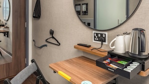 A compact hotel room with a foldable chair, a small wooden table, a coffee maker, a kettle, and a mirror on the wall. - Point A Dublin The Liberties (Dublin)