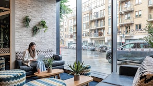 A modern interior with a woman working on a laptop, large windows, and a view of the street. - Point A Dublin The Liberties (Dublin)