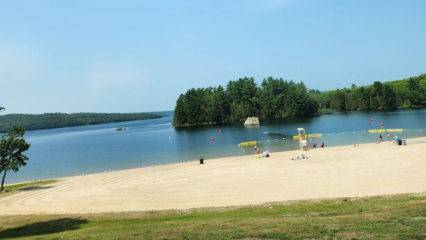A beach with a sandy shore, a small island with trees, and a calm lake.
