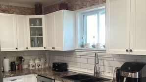A modern kitchen with white cabinets, a granite countertop, a built-in dishwasher, and a coffee maker.