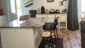 A kitchen with a granite countertop, a bar stool, a coffee maker, and a clock on the wall.