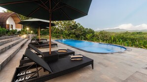 A poolside area with lounge chairs and umbrellas, a clear view of the pool, and steps leading to a house.