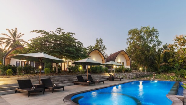 A swimming pool with lounge chairs and umbrellas, surrounded by greenery and a stone wall.