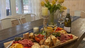 Una mesa de madera con una tabla de fiambres, un florero con tulipanes amarillos y una botella de vino.