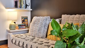 Un dormitorio acogedor con una cama, una mesita de noche con libros, una lámpara y una pared decorada con cuadros.