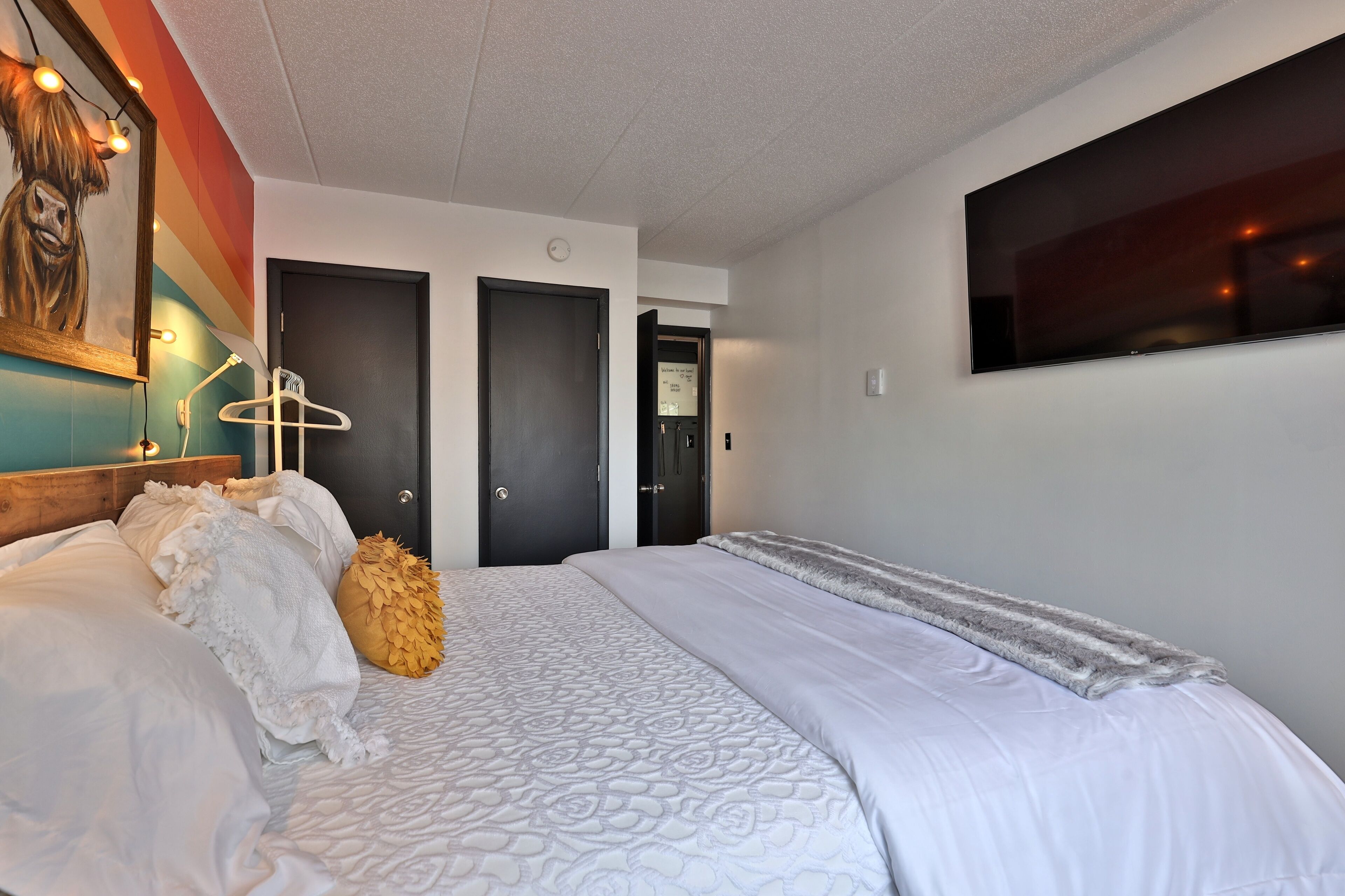 A hotel room with a large bed, a TV mounted on the wall, and a painting on the wall.