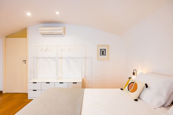 A bedroom with a bed, a wardrobe, a window with curtains, an air conditioning unit, and a wall-mounted light fixture.