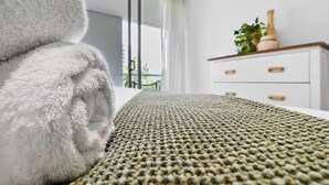 Una cama bien hecha con un edredón texturizado, un aparador blanco con cajones y una planta en maceta encima.