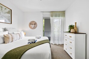 A neatly arranged bedroom with a bed, bedside table, and a dresser. - Coastal Harbour Lights -pool Gym Prime Location (Cairns)