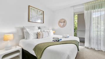 Habitación de hotel con una cama bien hecha, una lámpara de noche, una obra de arte enmarcada y vistas a zonas verdes a través de la ventana.