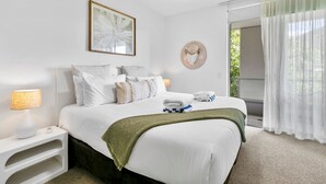 Een hotelkamer met een netjes opgemaakt bed, een bedlampje, een kunstwerk in een lijst en uitzicht op groen door het raam.
