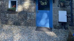 Un edificio de piedra con una puerta azul, una pequeña ventana adornada con flores y un adorno en la puerta.