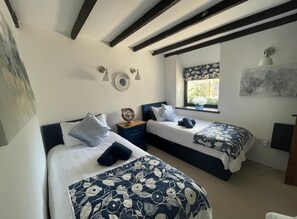 Een kamer met twee bedden, elk voorzien van een bloemenbedekking, een nachtkastje met een klok en een raam met uitzicht op groen.
