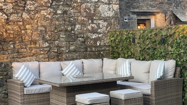 Un área de estar al aire libre con muebles de mimbre, una mesa con superficie de vidrio y bancos acolchados.