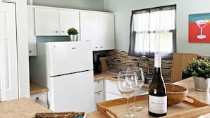 Una cucina moderna con mobili bianchi, forno a microonde integrato e un piano di lavoro in legno. Su un vassoio in legno, si trova una bottiglia di vino e due bicchieri.
