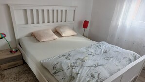 Siististi pedattu sänky, jossa on kukkakuviollinen päiväpeite, valkoinen pääty ja kaksi tyynyä.