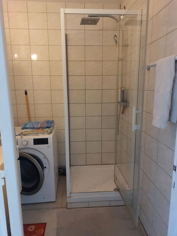 A small bathroom with a glass-enclosed shower, a washing machine, and a towel rack.