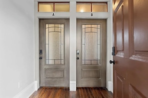 Two wooden doors with frosted glass panels, labeled A and B, with a white wall and wooden flooring in the background. - Luxury Casa B
(Savannah)