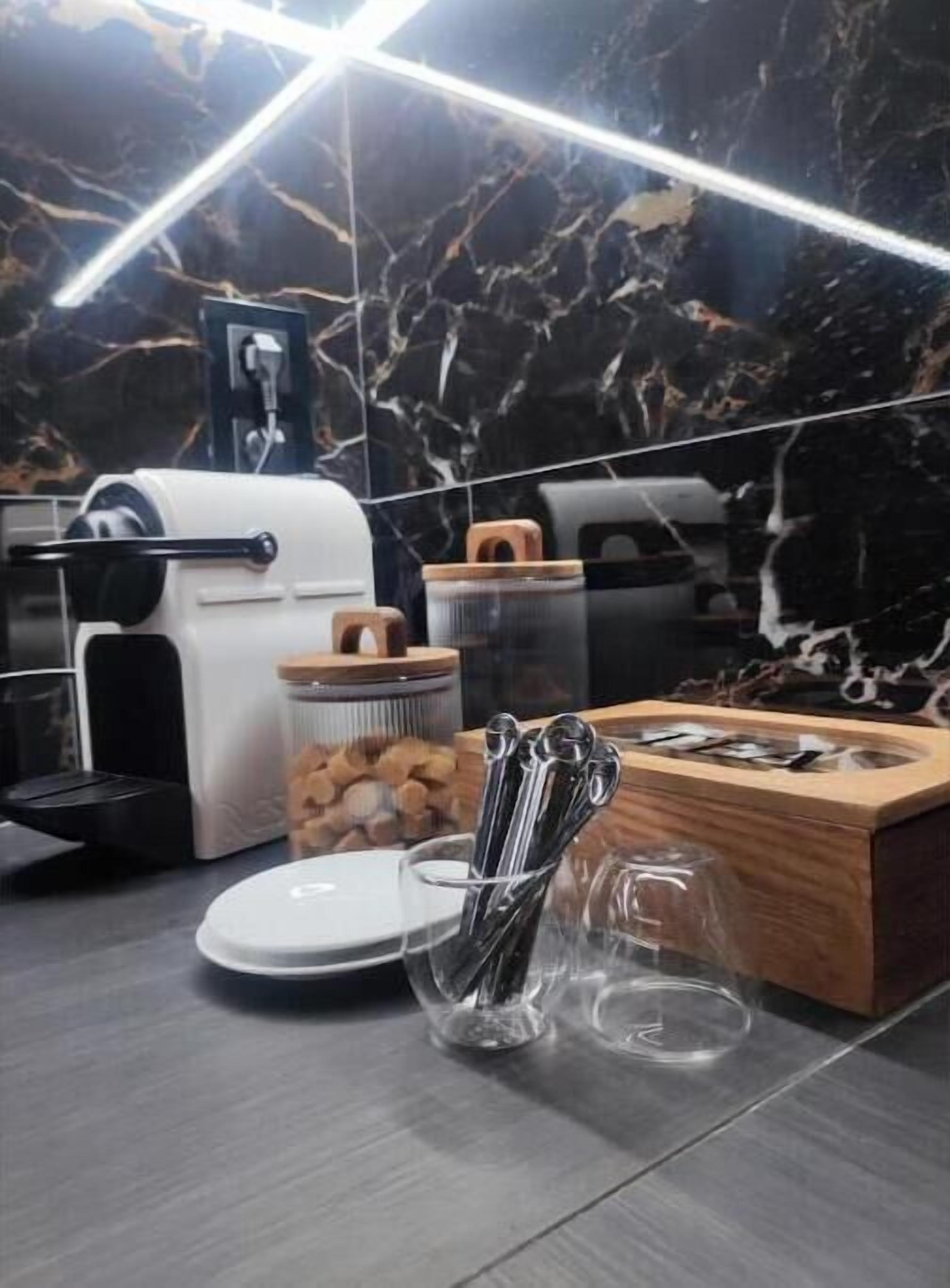 Een keuken met een marmeren spatwand, een koffieapparaat, een keukenmachine, een houten snijplank en diverse keukengerei.