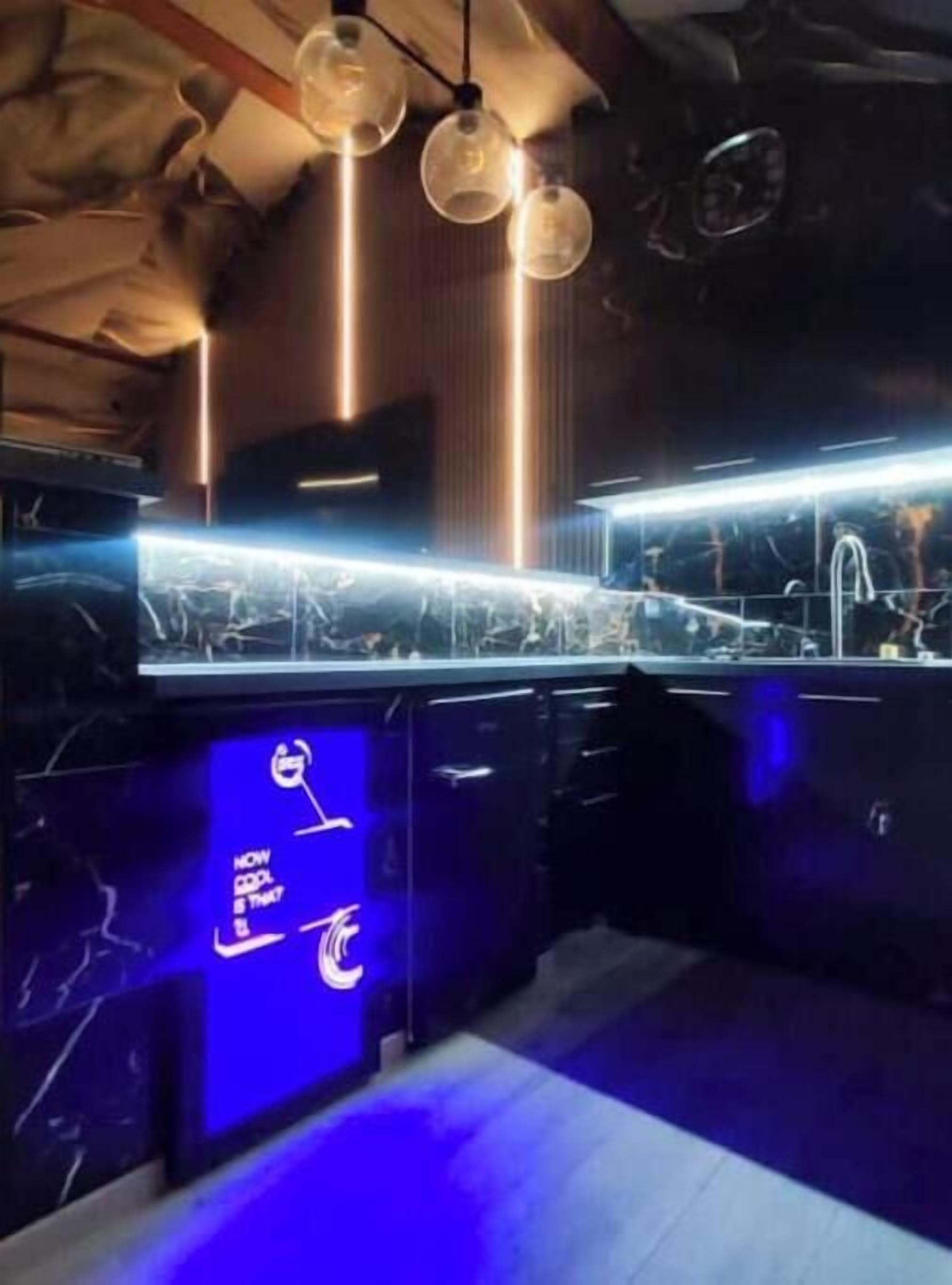A bar area with a counter, hanging light fixtures, and a blue illuminated sign.