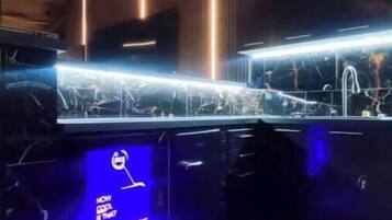 A bar area with a counter, hanging light fixtures, and a blue illuminated sign.