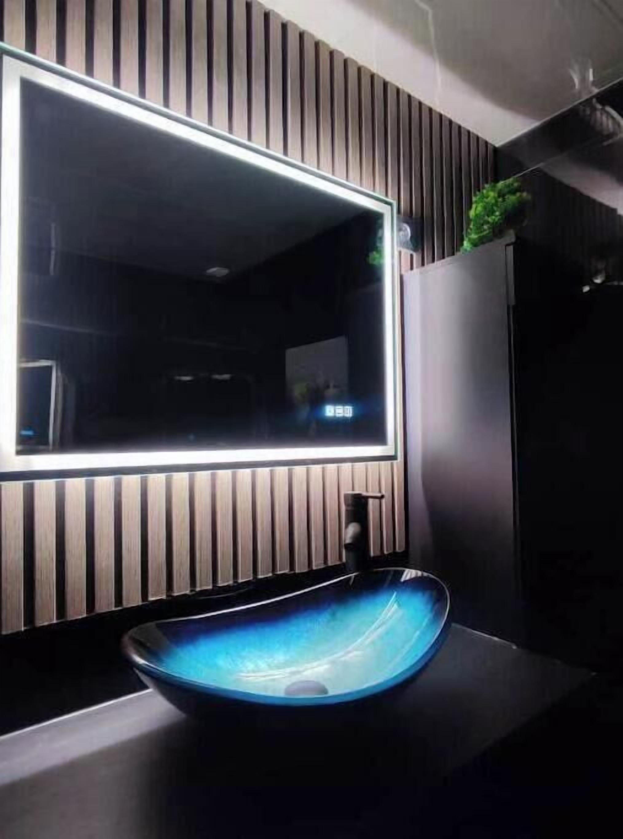 A modern bathroom with a large mirror, a blue vessel sink, and vertical wooden paneling on the wall.