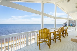 A covered deck with wooden chairs and a view of the ocean.