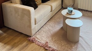 A living room with a beige sofa, two black and one multicolored cushion, a white coffee table, and a patterned rug.
