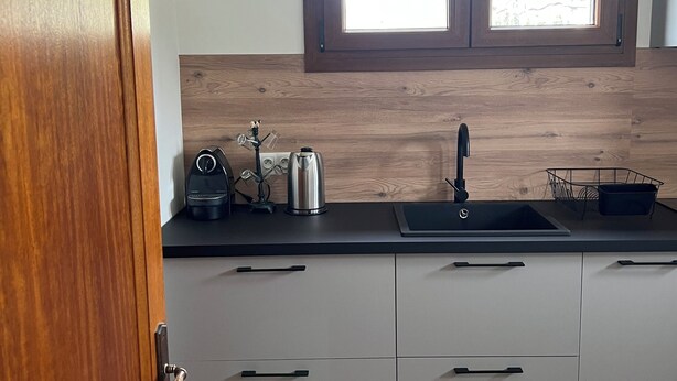 A kitchen with a wooden door, a window, a sink, and a kettle on the countertop.