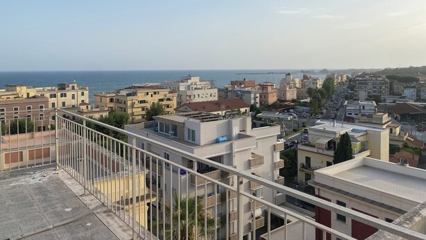 Un paysage urbain côtier avec vue sur la mer, comprenant divers bâtiments et un ciel dégagé.