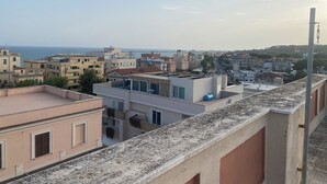 A residential area with buildings of various heights and architectural styles, a clear sky, and a distant view of the sea. - Casa Nettuno (Nettuno)