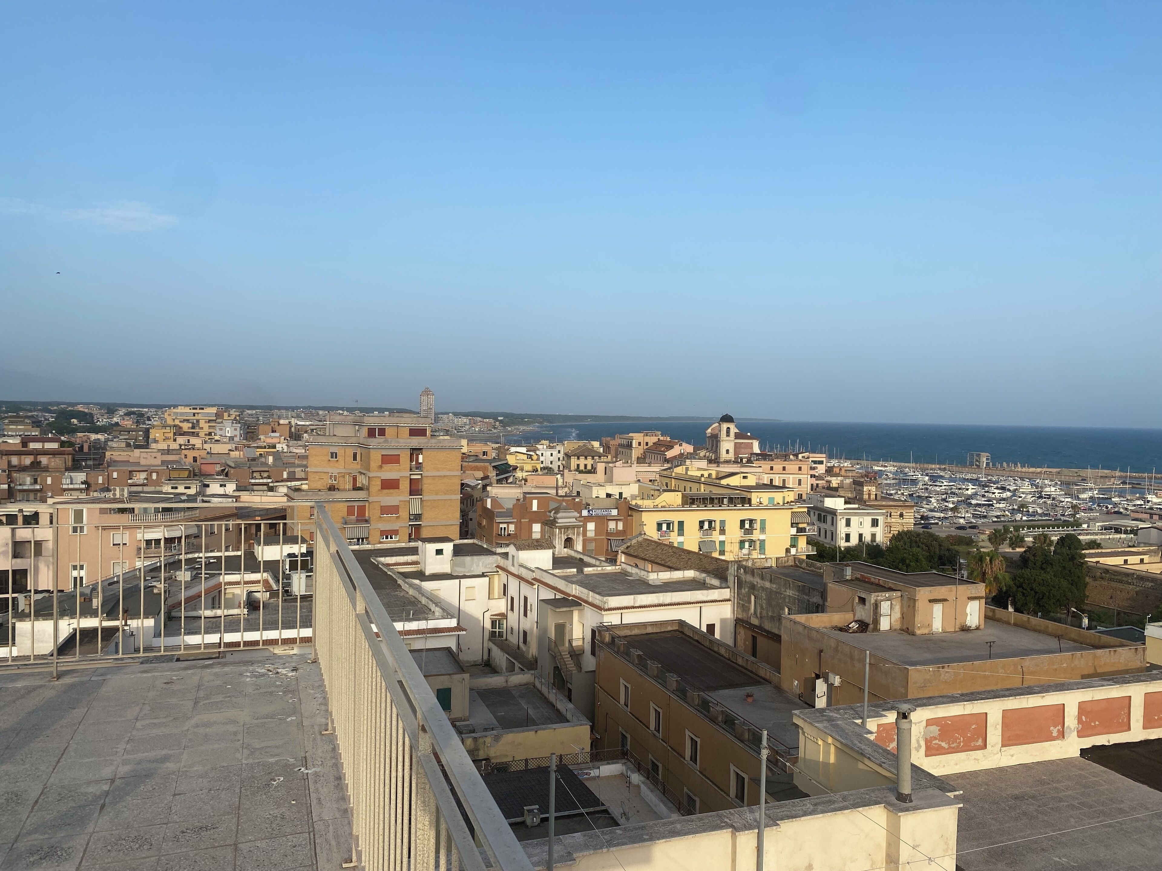 Un paysage urbain côtier avec des bâtiments, un port de plaisance et un ciel dégagé.