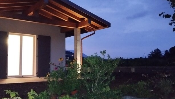 A modern house with a wooden pergola, a well-lit window, and a garden with various plants and rocks. - Memi's Home - Family villa whit big exclusive garden, 7 km from Salò, Garda Lake (San Biagio)