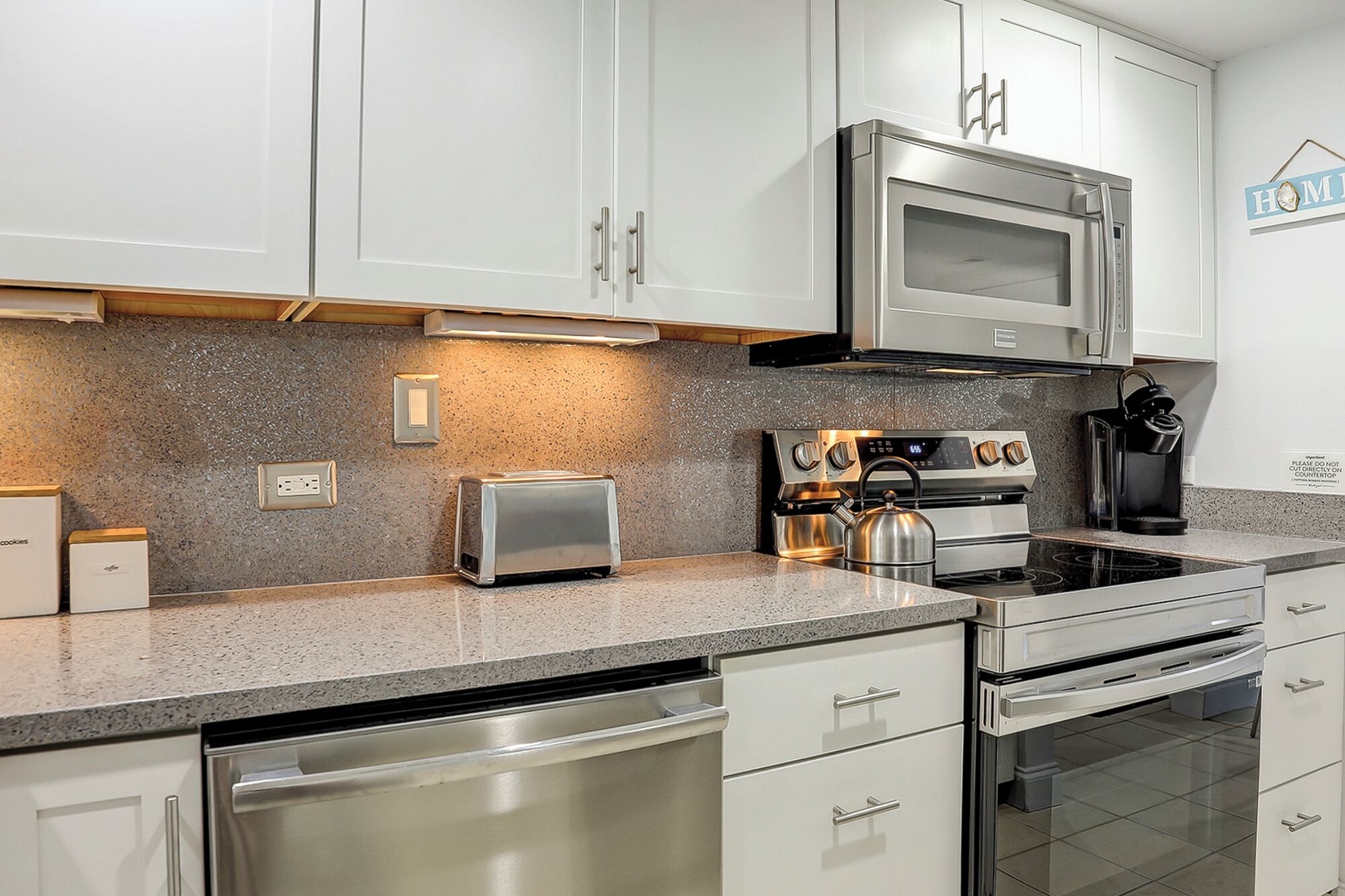 A modern kitchen with white cabinetry, a stainless steel microwave, a toaster, a kettle, and a dishwasher.