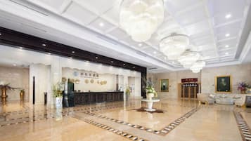 Een hotel lobby met een receptiebalie, een kroonluchter en een vloer met patroon.
