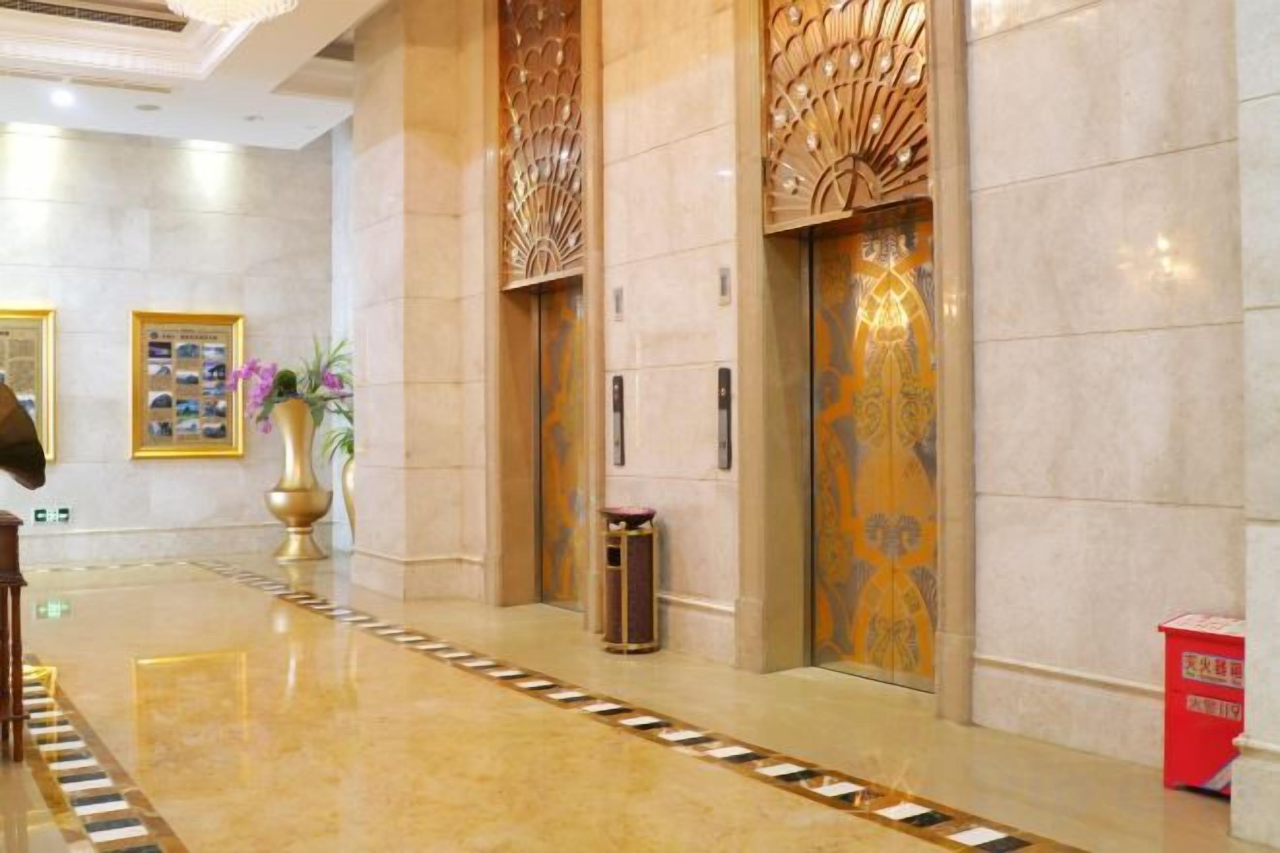 Um saguão de hotel com piso lustroso, painéis decorativos na parede e uma lixeira.