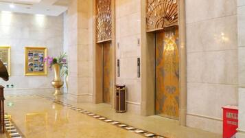 Um saguão de hotel com piso lustroso, painéis decorativos na parede e uma lixeira.