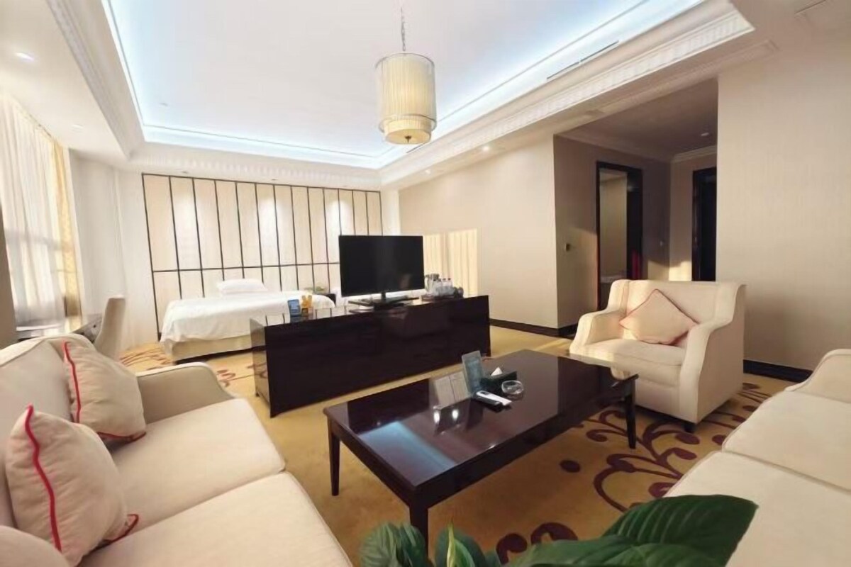 A hotel room with a bed, a television, a sofa, a coffee table, and a chair.