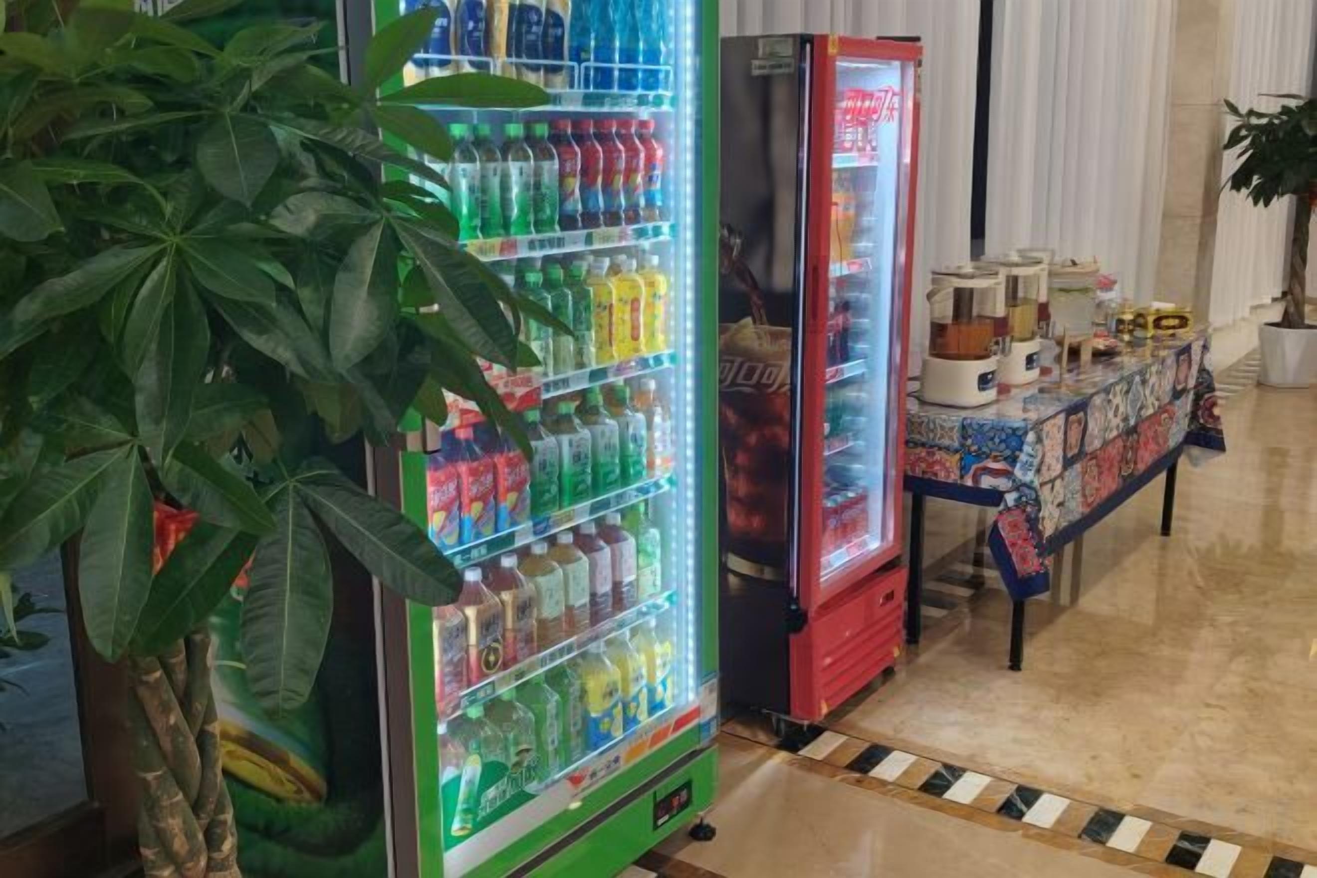A vending machine with various drinks and a table with items on it.