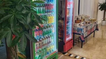 A vending machine with various drinks and a table with items on it.