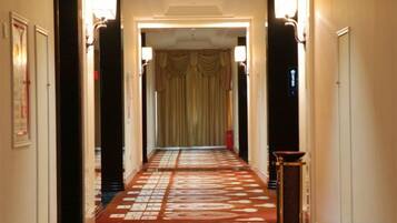A hallway with a patterned carpet, wall sconces, and a door at the end.