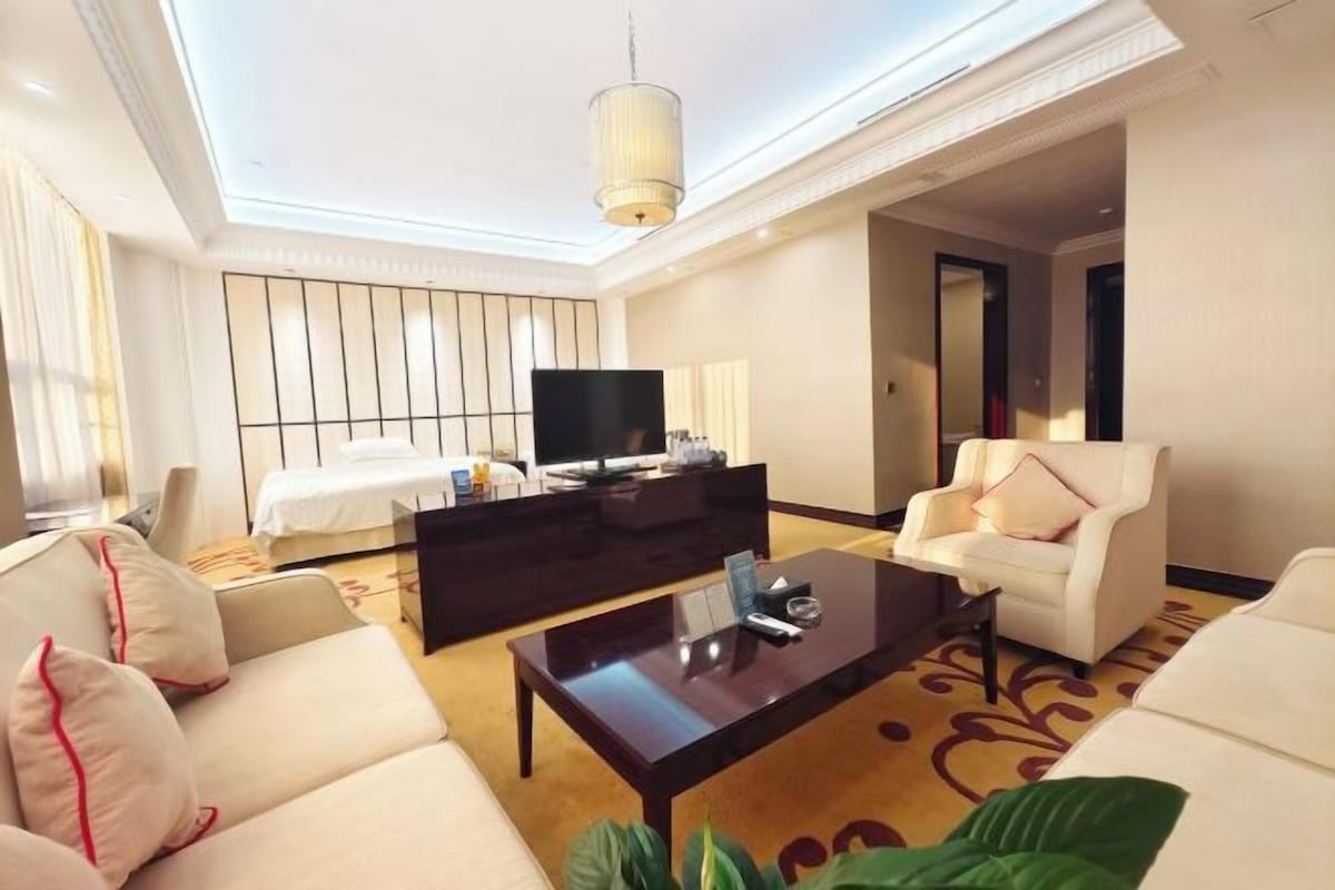 A hotel room with a bed, a TV, a sofa, a coffee table, and a chair.