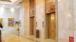 A polished lobby with marble flooring, a central column, and two elevators with ornate doors.