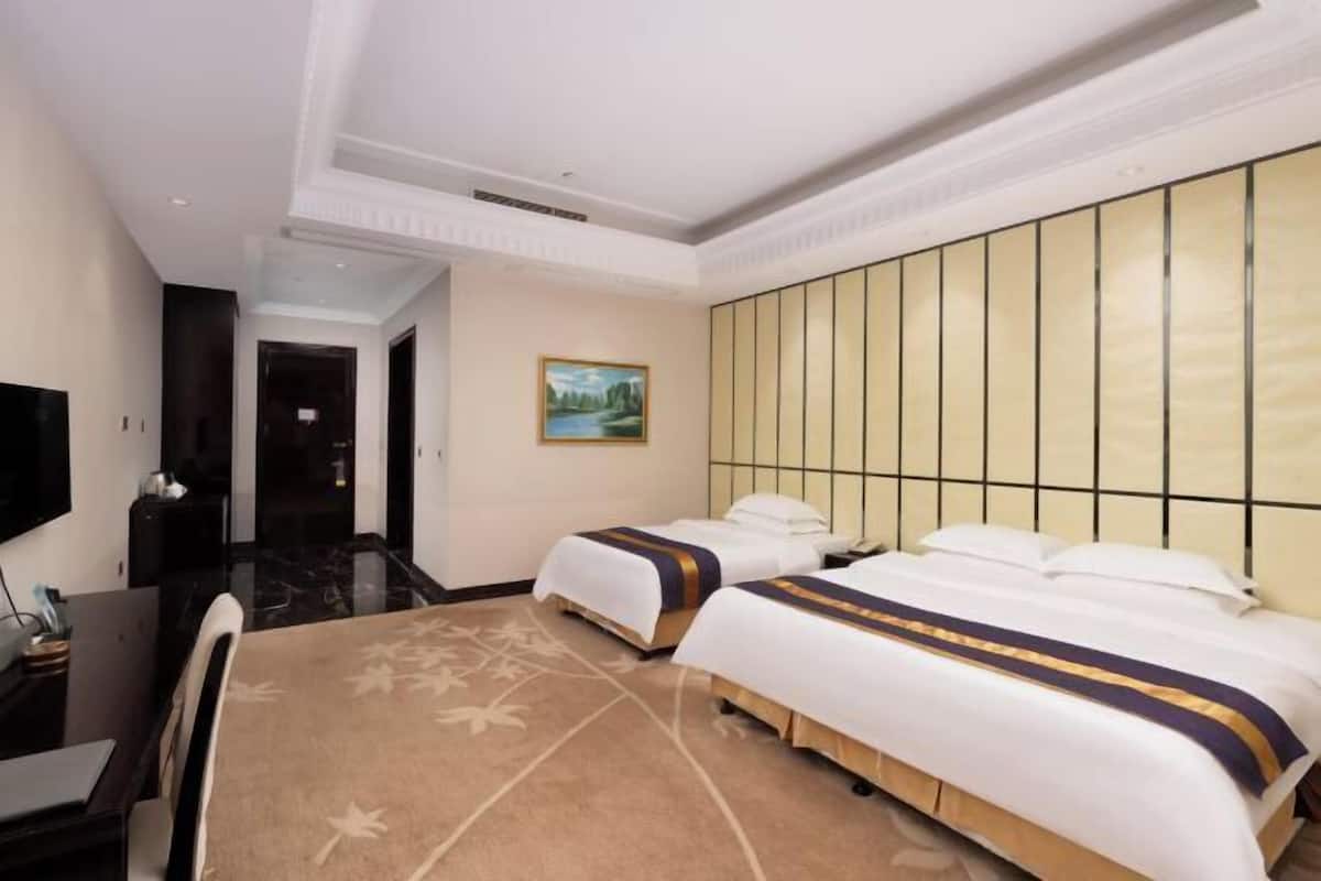 A hotel room with two beds, a TV, a desk, and a painting on the wall.