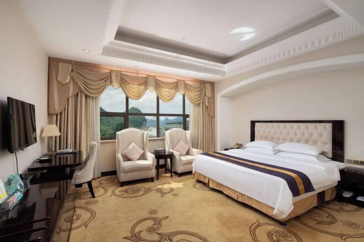 A hotel room with a large bed, two armchairs, a desk, and a television.