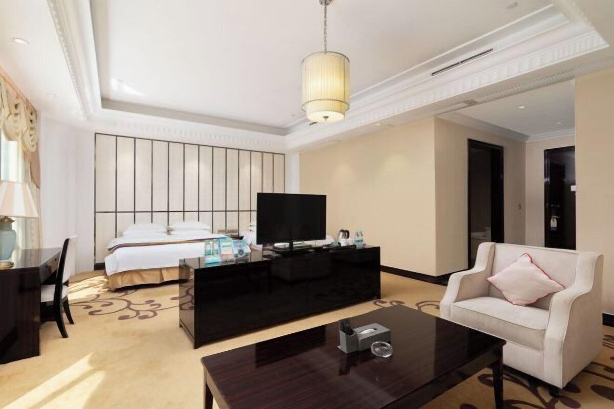 A modern hotel room with a bed, a black entertainment unit, a white sofa, a coffee table, and a television.