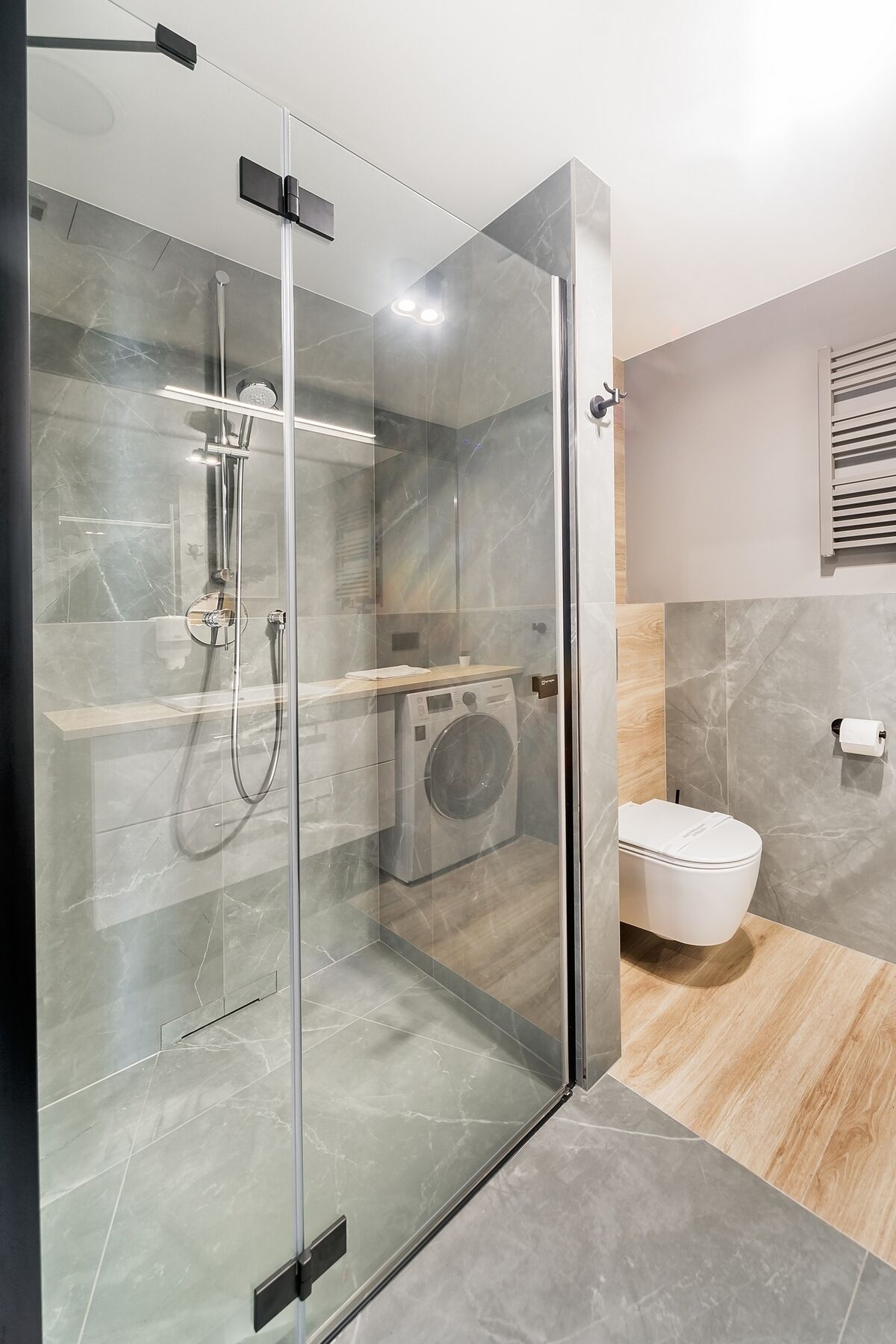 Un baño moderno con ducha envuelta en vidrio, lavadora integrada y un inodoro.