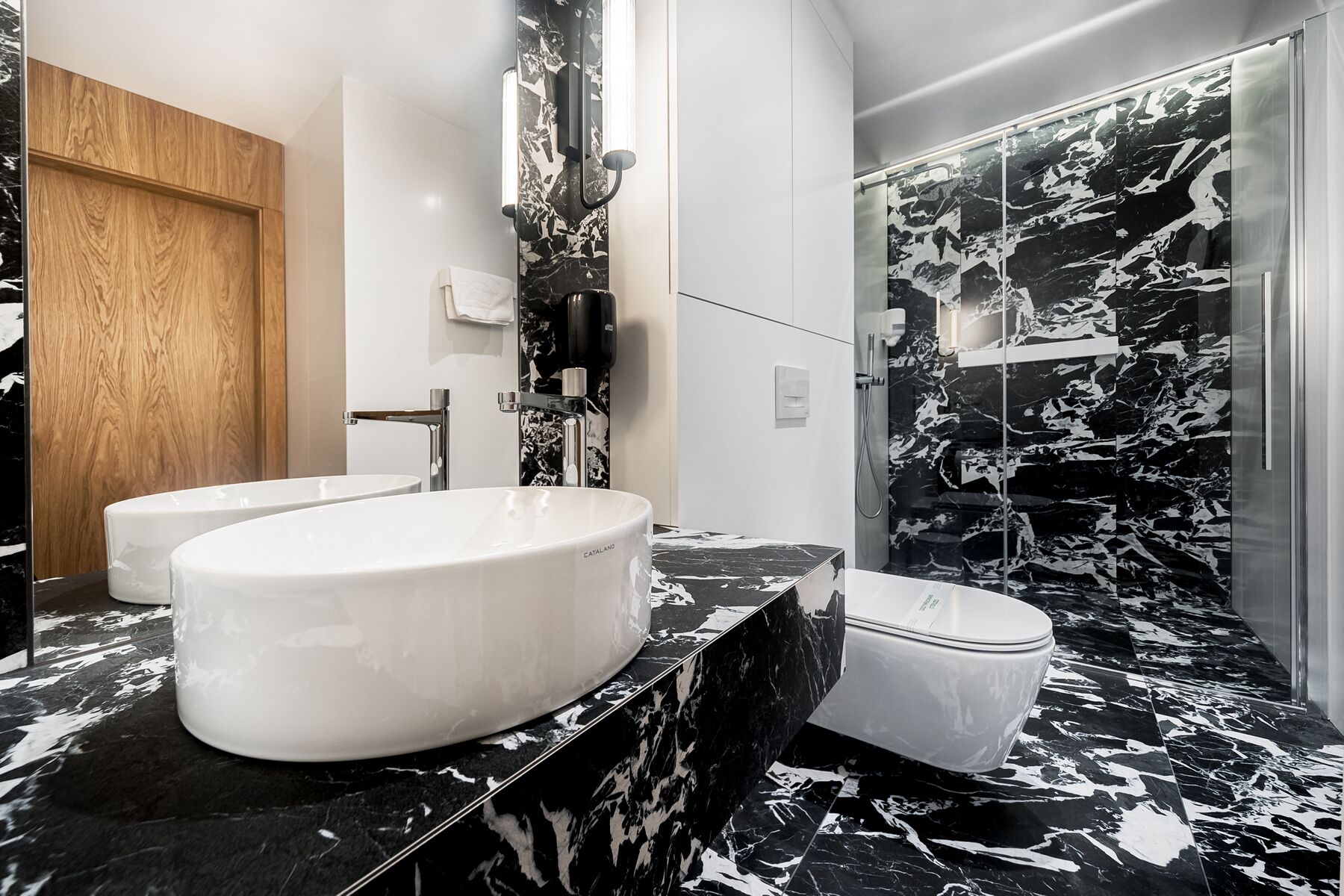 A modern bathroom with a large white sink, a toilet, and a shower area with a black and white marble design.