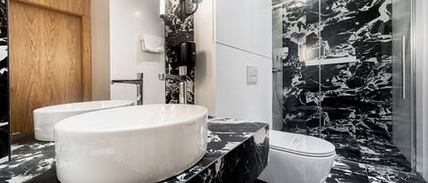 A modern bathroom with a large white sink, a toilet, and a shower area with a black and white marble design.